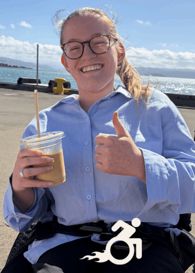 Daisy giving a thumbs up with an iced coffee by the waterfront