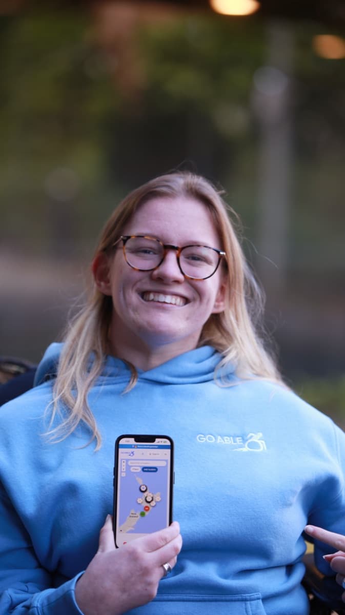 Daisy smiling in a Go Able hoodie, holding a phone showing the Go Able map app