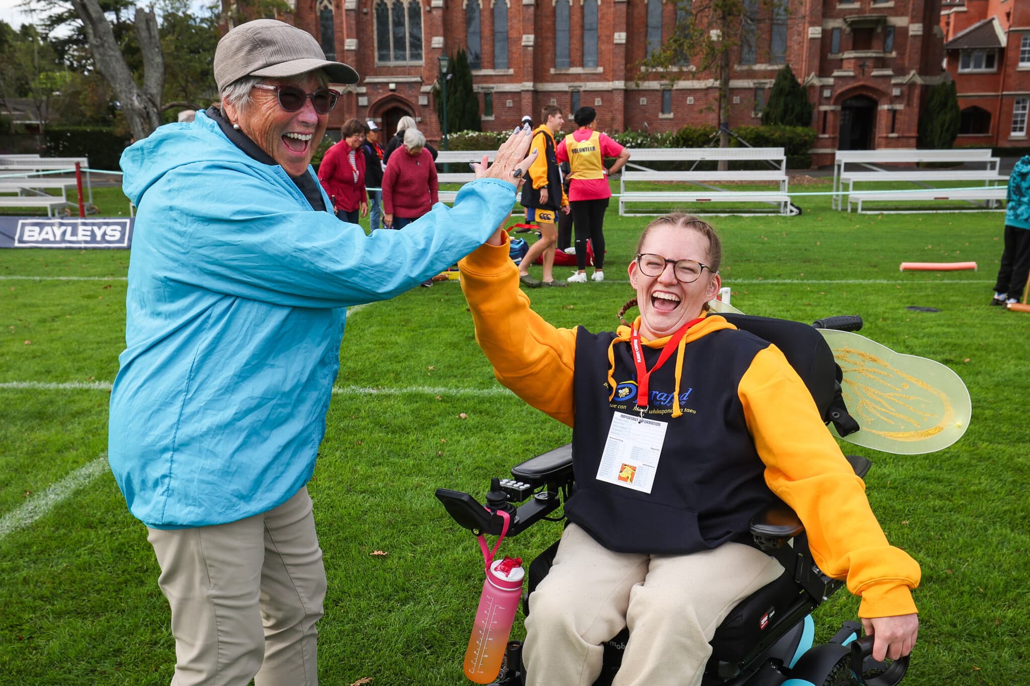 Daisy Hoe high-fiving at the Halberg Games, smiling in her wheelchair on a sports field